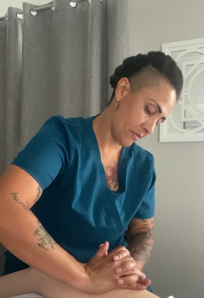 Woman in teal scrubs in a massage studio is massaging a person's leg.